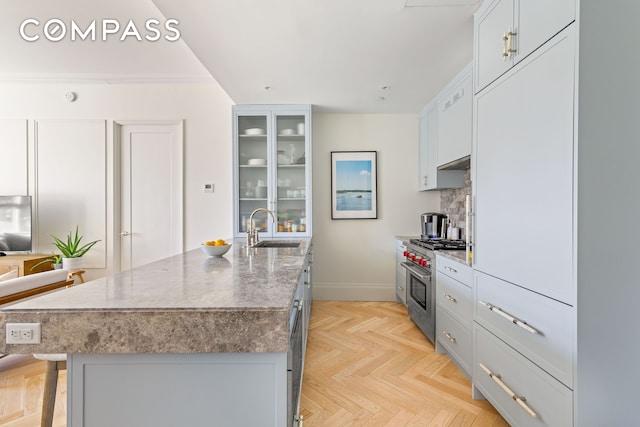 kitchen with a breakfast bar area, a sink, decorative backsplash, glass insert cabinets, and high end stainless steel range