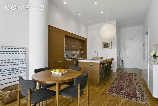 kitchen with sink, light hardwood / wood-style flooring, a kitchen island with sink, dark brown cabinets, and oven