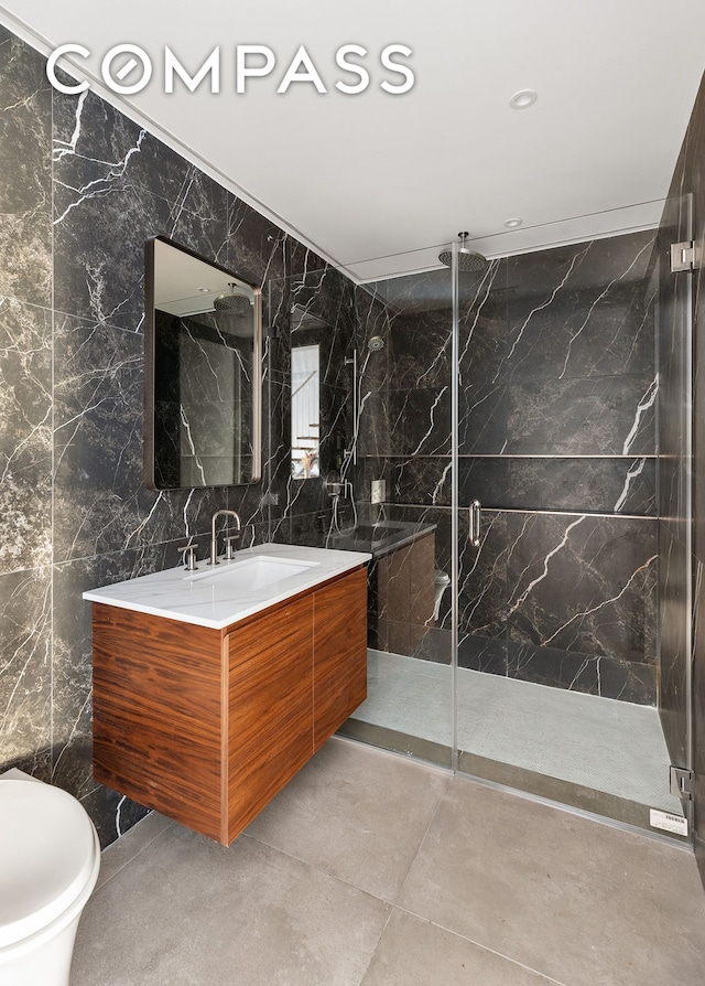 bathroom with a marble finish shower, toilet, vanity, and tile walls