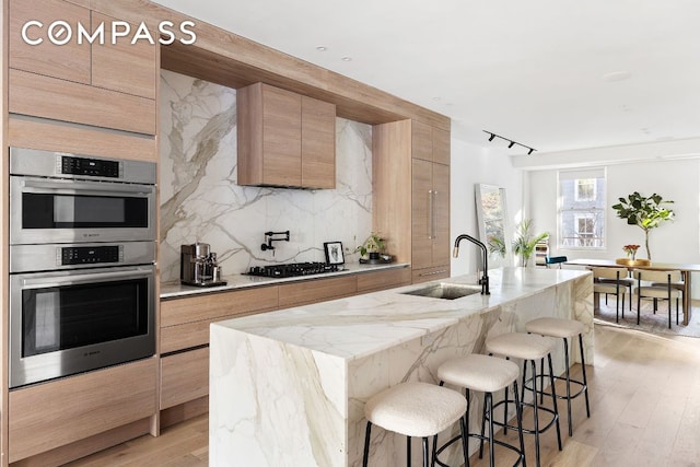 kitchen featuring double oven, a sink, a center island with sink, and modern cabinets