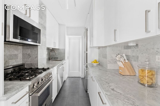 kitchen featuring sink, appliances with stainless steel finishes, backsplash, light stone countertops, and white cabinets