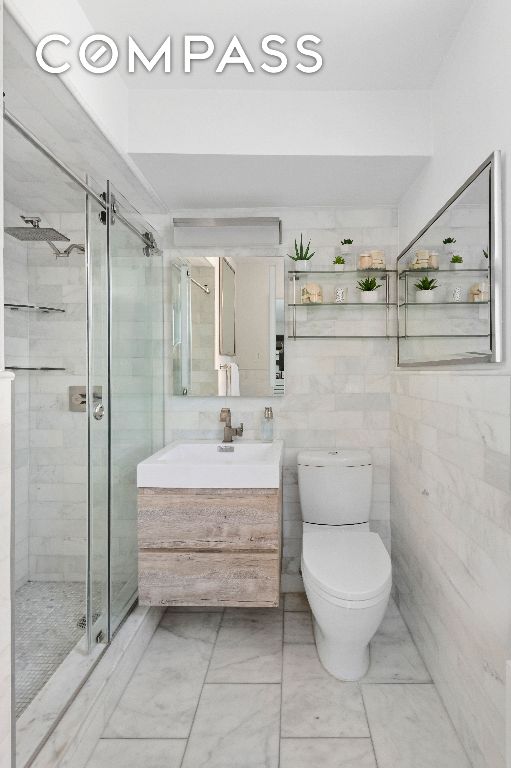 bathroom featuring a shower with door, vanity, tile walls, and toilet