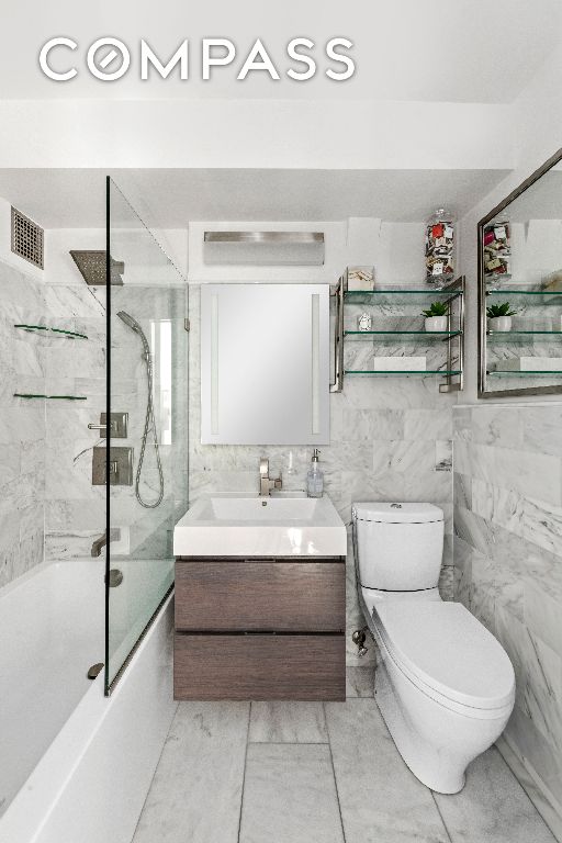 full bathroom featuring enclosed tub / shower combo, vanity, toilet, and tile walls