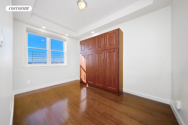 unfurnished bedroom featuring dark hardwood / wood-style flooring and a tray ceiling