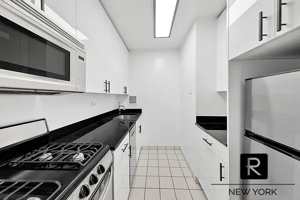 kitchen with white microwave, stainless steel range with gas stovetop, white cabinetry, and dark countertops