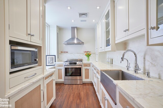 kitchen featuring decorative backsplash, light stone counters, stainless steel appliances, dark wood-type flooring, and wall chimney range hood