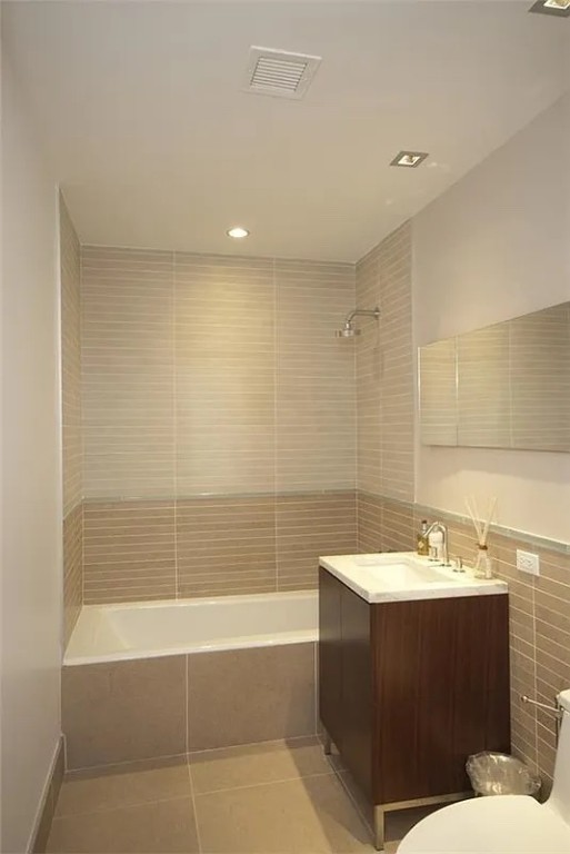 full bathroom featuring tile walls, tile patterned flooring, vanity, tiled shower / bath, and toilet