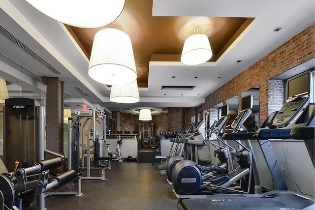 workout area featuring brick wall and a tray ceiling