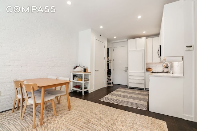 recreation room with white cabinetry, brick wall, wood-type flooring, and sink