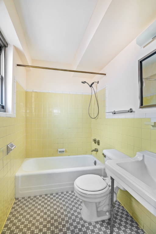 bathroom with tile patterned flooring, tiled shower / bath combo, tile walls, and toilet