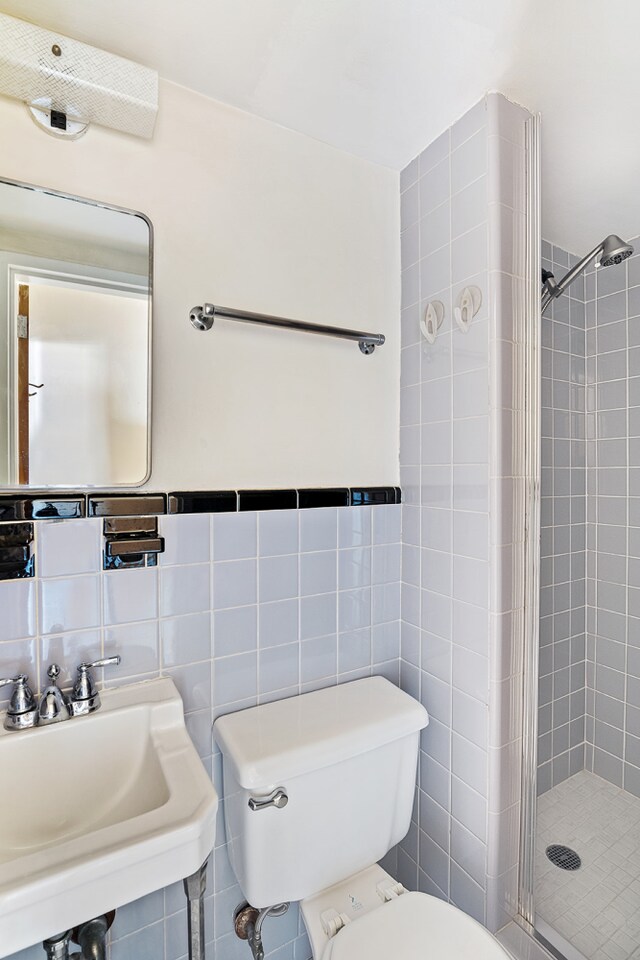 bathroom with walk in shower, toilet, sink, and tile walls