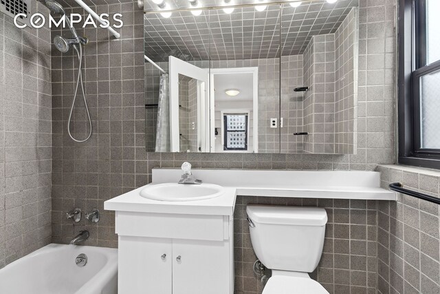 full bathroom with vanity, tile walls, shower / tub combo with curtain, and toilet