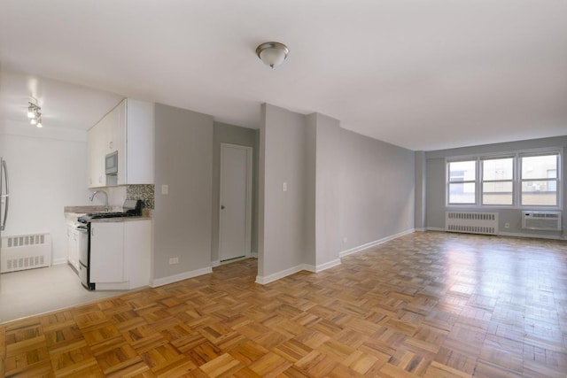 unfurnished living room featuring radiator heating unit, an AC wall unit, and light parquet floors