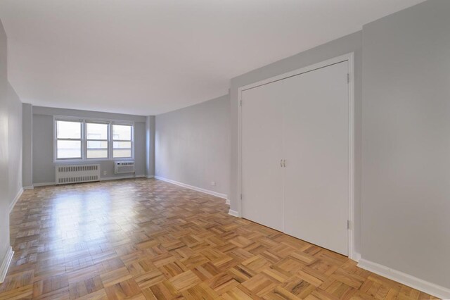 empty room featuring a wall mounted air conditioner, radiator, and light parquet floors