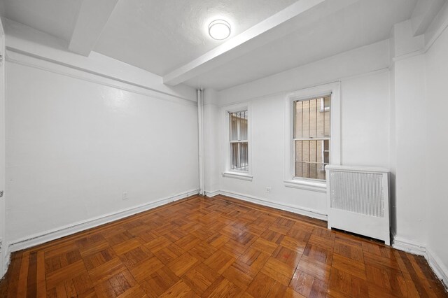 unfurnished room with parquet flooring, radiator heating unit, and beam ceiling