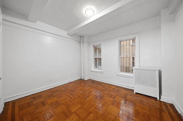 empty room featuring beam ceiling, baseboards, and radiator heating unit