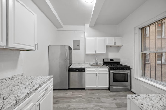 kitchen featuring light wood finished floors, light stone countertops, stainless steel appliances, white cabinetry, and a sink