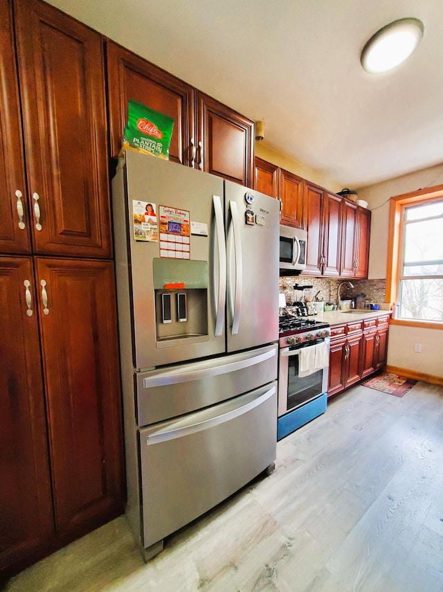kitchen featuring a sink, light wood-style floors, light countertops, stainless steel appliances, and tasteful backsplash