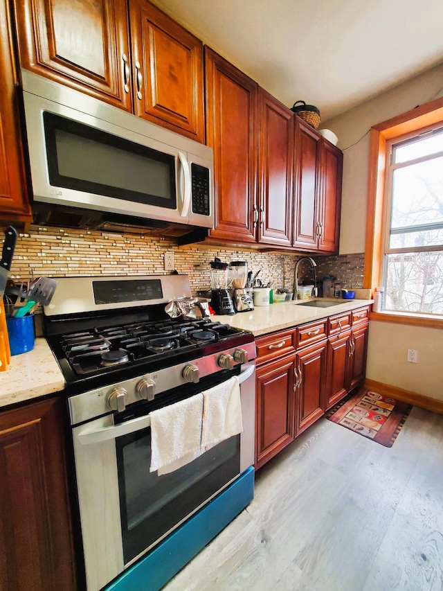 kitchen featuring dark brown cabinets, a sink, light wood finished floors, appliances with stainless steel finishes, and backsplash