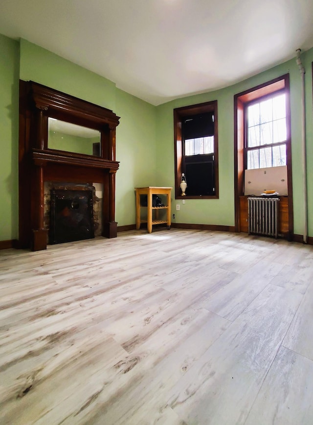unfurnished living room with radiator, baseboards, a fireplace, and wood finished floors