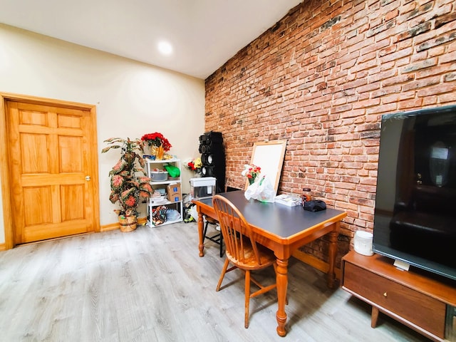 home office featuring baseboards, wood finished floors, and brick wall
