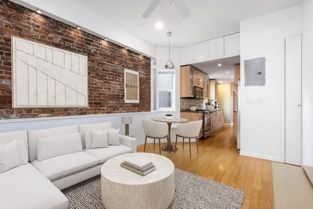 living area with ceiling fan, brick wall, baseboards, light wood-type flooring, and electric panel