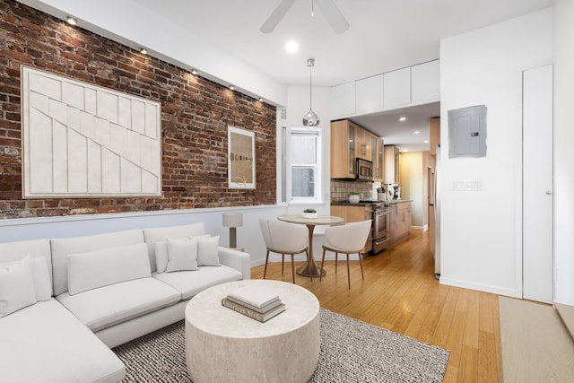 living area with baseboards, brick wall, electric panel, ceiling fan, and light wood-style floors