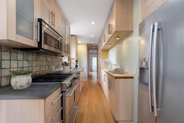 236 E 6th St Unit 5E, New York City, NY 10003 - kitchen with tasteful backsplash, appliances with stainless steel finishes, glass insert cabinets, a sink, and light wood-type flooring