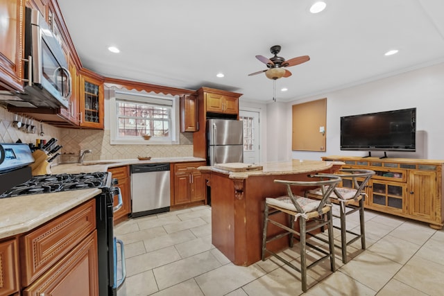 kitchen with crown molding, a breakfast bar area, stainless steel appliances, a kitchen island, and decorative backsplash