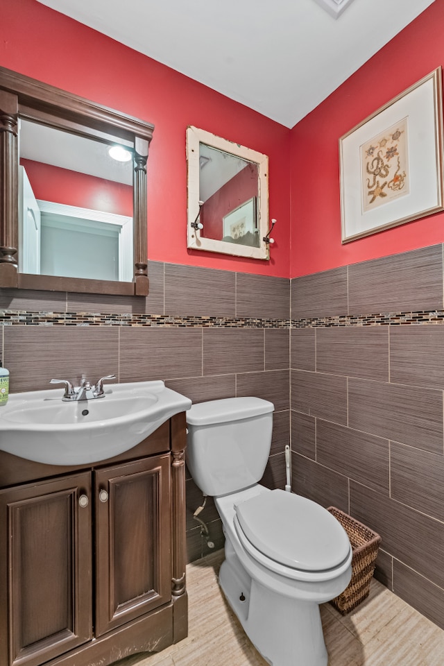 half bath featuring tile walls, toilet, vanity, and a wainscoted wall