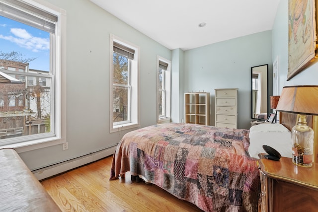 bedroom featuring a baseboard radiator, light hardwood / wood-style floors, and multiple windows