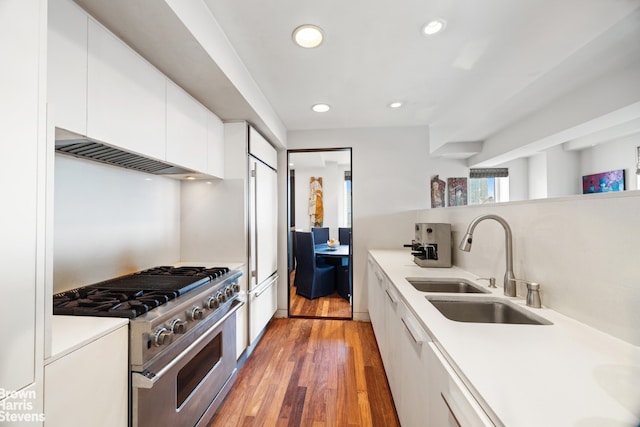 kitchen with light countertops, high end stove, a sink, white cabinetry, and light wood-type flooring