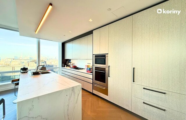 kitchen with gas cooktop, light parquet floors, double oven, light stone countertops, and a center island with sink