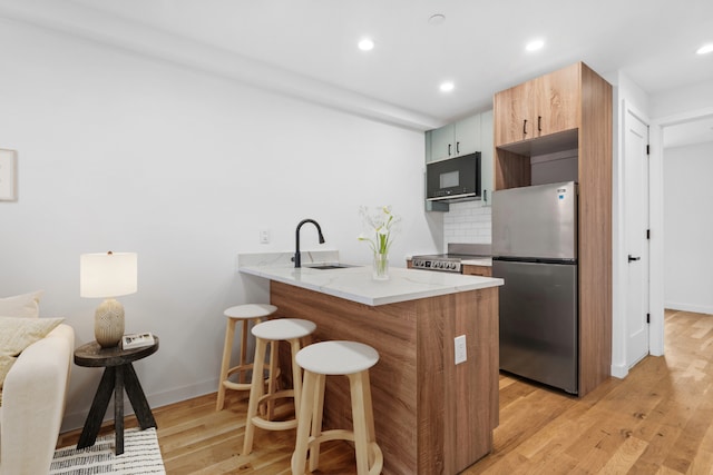 kitchen with light wood-type flooring, a sink, tasteful backsplash, appliances with stainless steel finishes, and a breakfast bar area