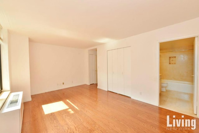 unfurnished bedroom with wood-type flooring, a closet, and ensuite bathroom