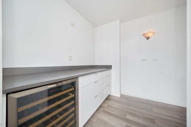 bar with white cabinets, beverage cooler, and light hardwood / wood-style floors