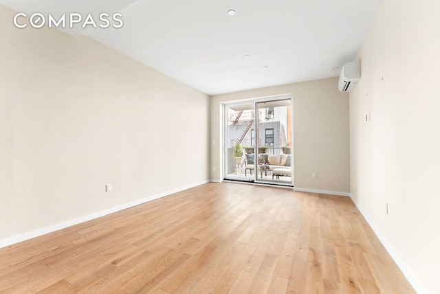 empty room with light wood-type flooring, a wall unit AC, and baseboards