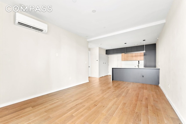 unfurnished living room featuring light wood-type flooring, a sink, baseboards, and a wall mounted AC