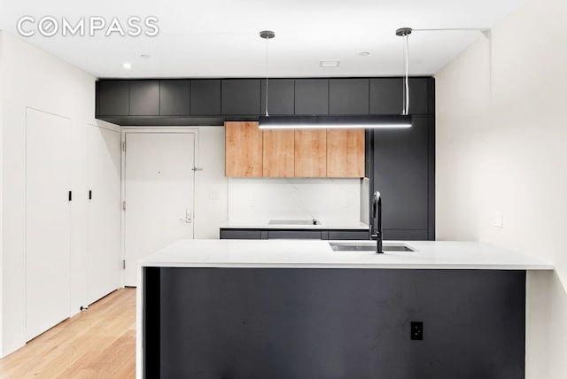 kitchen with hanging light fixtures, sink, backsplash, and light hardwood / wood-style floors