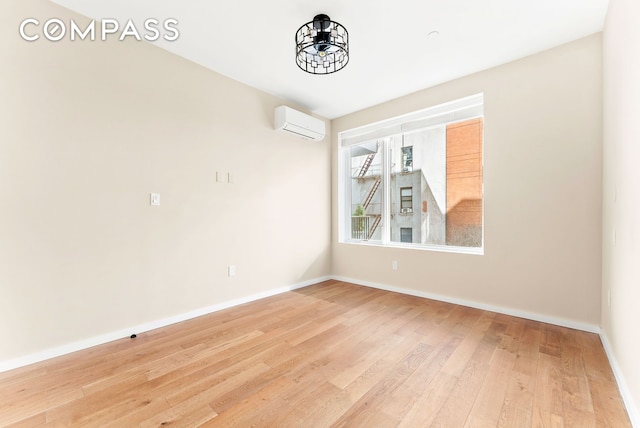 spare room with baseboards, an AC wall unit, and wood finished floors