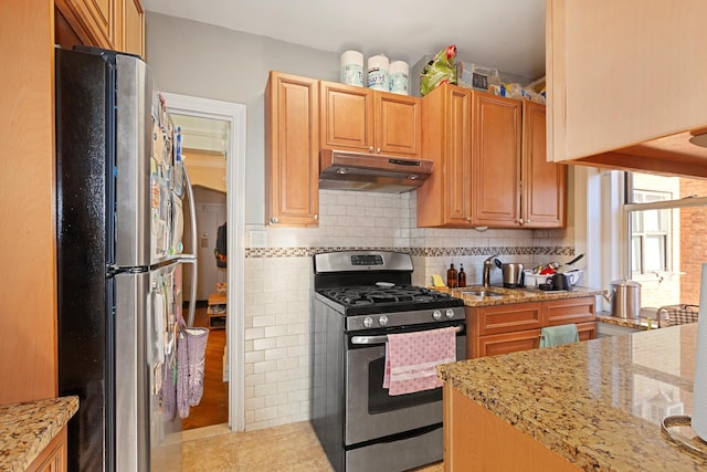 kitchen with under cabinet range hood, decorative backsplash, appliances with stainless steel finishes, and light stone counters