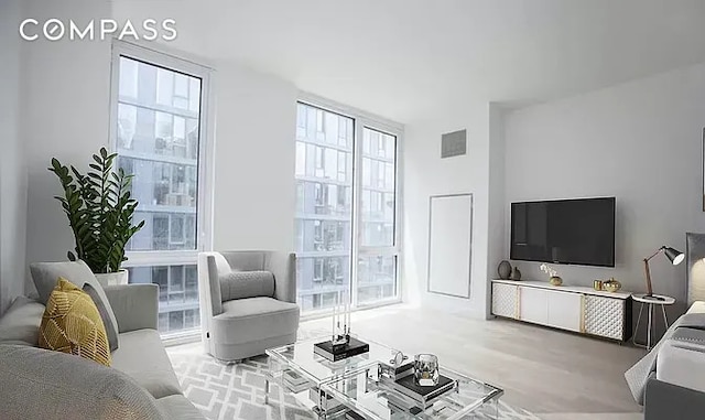 living area with floor to ceiling windows, wood finished floors, visible vents, and a wealth of natural light