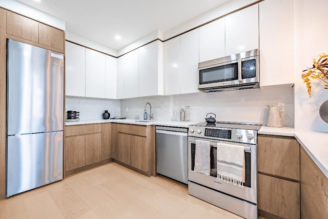 kitchen with sink, backsplash, stainless steel appliances, white cabinets, and light wood-type flooring