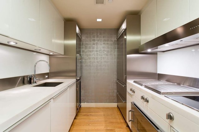 kitchen with sink, white cabinets, light hardwood / wood-style floors, and wall chimney exhaust hood