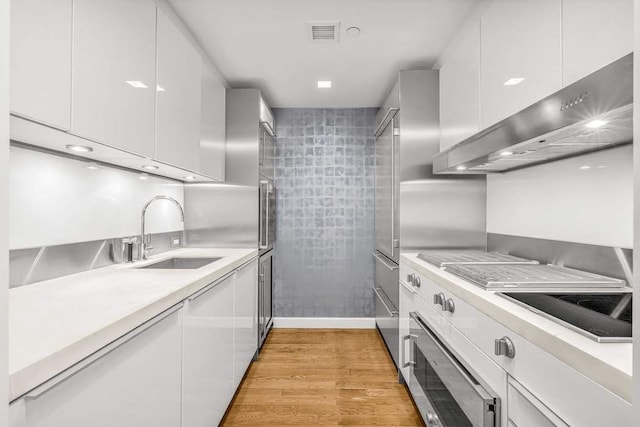 kitchen featuring white cabinets, light countertops, a sink, and wall chimney range hood