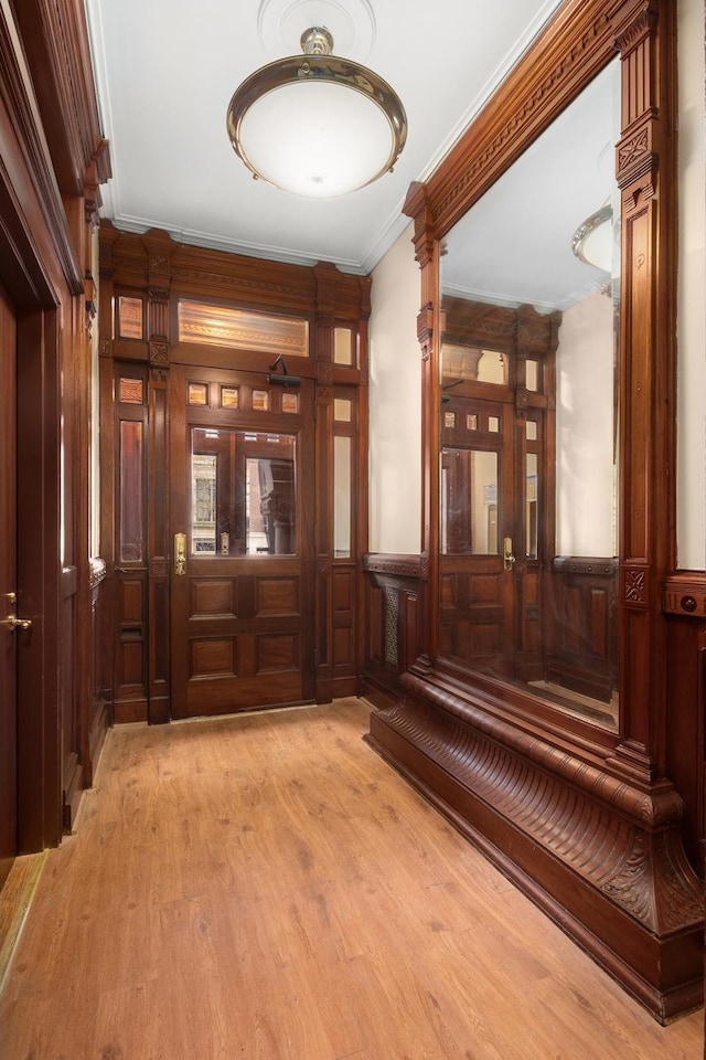 foyer entrance with a wainscoted wall, crown molding, and light wood-style floors