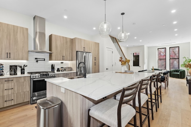 kitchen featuring appliances with stainless steel finishes, light brown cabinets, a sink, wall chimney range hood, and modern cabinets