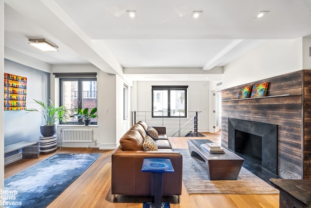 living room with beam ceiling, hardwood / wood-style flooring, radiator heating unit, and a high end fireplace