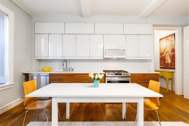 kitchen featuring appliances with stainless steel finishes, dark hardwood / wood-style floors, white cabinetry, sink, and beam ceiling