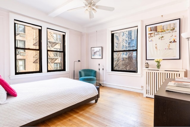 bedroom with radiator heating unit, ceiling fan, beamed ceiling, light wood finished floors, and baseboards